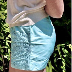 May include: A light blue embroidered skirt with a white top tucked in. The skirt has a floral design.