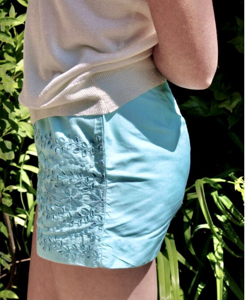 May include: A light blue embroidered skirt with a white top tucked in. The skirt has a floral design.