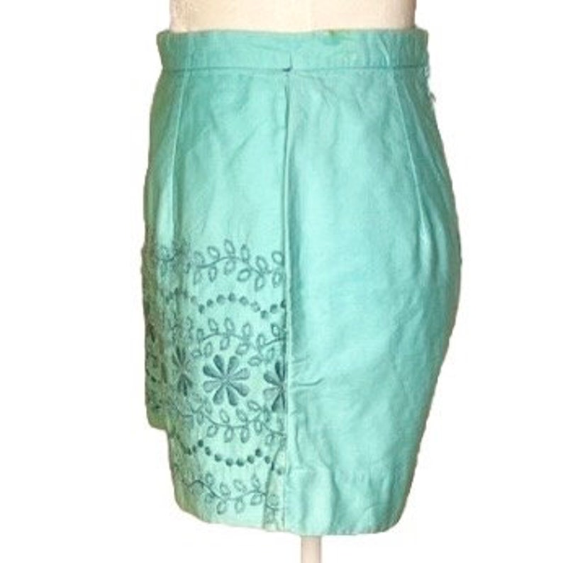 May include: A turquoise blue skirt with embroidered floral details around the bottom hem.