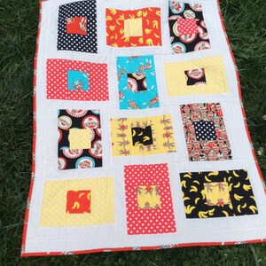 May include: A white baby quilt with a red, yellow, and blue patchwork design. The quilt features a variety of monkey-themed fabrics, including monkeys wearing socks, monkeys with bananas, and monkeys with polka dots.