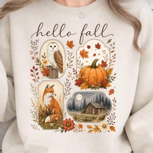 May include: A beige crewneck sweatshirt featuring the text hello fall in cursive script. The graphic includes four framed illustrations: a barn owl on a post, an orange pumpkin with autumn leaves, a red fox, and a cabin in a forest at night.