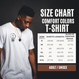 K&ouml;nnte beinhalten: Ein wei&szlig;es T-Shirt mit einer kleinen schwarzen Gl&uuml;hbirnengrafik auf der Brust. Daneben befindet sich eine Gr&ouml;&szlig;entabelle f&uuml;r Comfort Colors T-Shirts, die die Gr&ouml;&szlig;en S bis 3XL mit Ma&szlig;en in Zoll f&uuml;r Breite, L&auml;nge und &Auml;rmelmitte am R&uuml;cken auflistet.