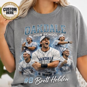 May include: A grey t-shirt featuring a graphic print of Oakdale High School baseball players in white uniforms. The design includes the text Oakdale High School and the name Brett Holden with the number 8, set against a blue lightning background.