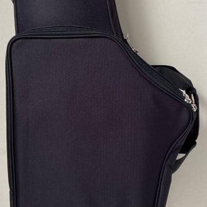 May include: Black instrument case with a silver logo and the text "TKL." The case has a zippered main compartment and a smaller compartment on top. A reflective orange stripe accents the bottom.