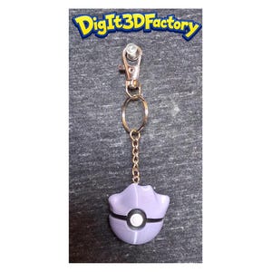 May include: A purple and white keychain featuring a stylized design. The keychain has a gold-colored chain and clasp. The text "Digit3DFactory" is visible at the top of the image.