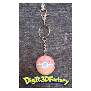 May include: A keychain featuring a pink and tan ball with blue and white accents, attached to a silver chain and clasp. The keychain has a decorative design and the text "Digit3DFactory" in a colorful font.