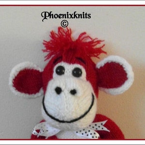 May include: A red and white knitted monkey toy with a white bow. The monkey has a red head with white ears and a white face with black eyes and a black smile.