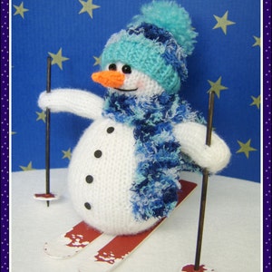 Puede incluir: Un muñeco de nieve de punto blanco que lleva un gorro y una bufanda azules y turquesa, sosteniendo bastones de esquí y de pie sobre esquís rojos y blancos sobre un fondo azul con estrellas blancas.
