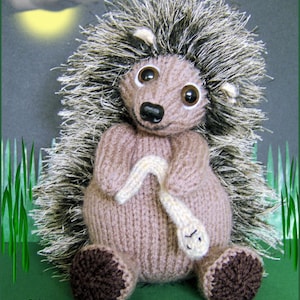 May include: A brown and gray knitted hedgehog toy with a white worm in its paws. The hedgehog is sitting on a green surface with white flowers.