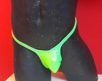 May include: A neon green thong swimsuit on a black mannequin. The swimsuit has a shiny, reflective finish and a thin, green string waistband. The background is a solid red color.