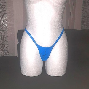May include: A blue thong swimsuit displayed on a white mannequin torso. The swimsuit has a simple design with thin straps and a low-rise cut. The mannequin is positioned against a neutral background.
