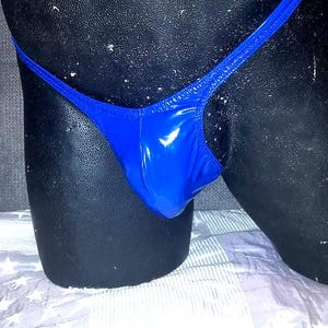 Könnte beinhalten: Ein glänzender, königsblauer String-Badeanzug-Unterteil. Der Stoff hat ein glänzendes Aussehen. Das Kleidungsstück wird auf einer schwarzen Schaufensterpuppe präsentiert. Der Hintergrund ist eine weiß-grau gemusterte Oberfläche.