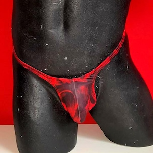 Op de afbeelding: Een zwarte mannequin torso draagt een rood en zwart patroon string. De string heeft een string tailleband en bedekt de voorkant. De achtergrond is rood.