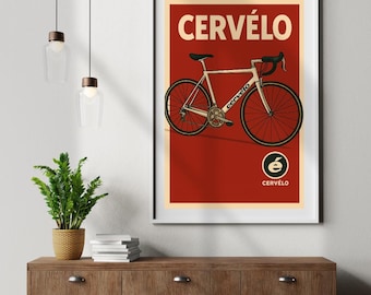 Op de afbeelding: Een ingelijste poster met een witte Cervélo racefiets op een rode achtergrond. Het woord "CERVÉLO" staat in grote, beige letters bovenaan, met het merklogo en de naam onderaan. De poster zit in een witte lijst.