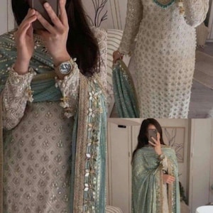 May include: A light beige embroidered dress with long sleeves, accompanied by a teal shawl. The shawl is decorated with gold and floral details. A gold wristwatch is visible on the wrist.