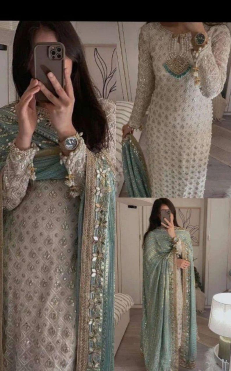 May include: A light beige embroidered dress with long sleeves, accompanied by a teal shawl. The shawl is decorated with gold and floral details. A gold wristwatch is visible on the wrist.