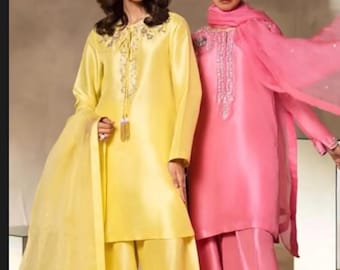 May include: Two women's outfits are shown. One is a bright yellow silk tunic and wide-leg trousers, with a sheer scarf. The other is a pink silk tunic and wide-leg trousers, with a matching scarf. Both outfits have decorative embellishments.