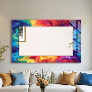 May include: A large rectangular wall mirror with a vibrant, colorful border. The border features a swirling pattern of rainbow hues, including red, orange, yellow, green, blue, and purple. The mirror is displayed above a white sofa in a living room setting.