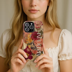 May include: A phone case featuring a floral design with red, yellow, and purple flowers. The word "MADELINE" is printed vertically on the right side of the case. The case has a glossy finish and a camera cutout.