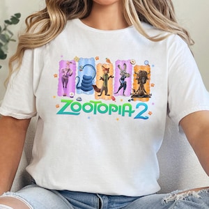 May include: White t-shirt featuring the text "Zootopia 2" in green and blue. The shirt has a colorful graphic of characters from the movie. The word "WHITE" is printed in white at the bottom right.