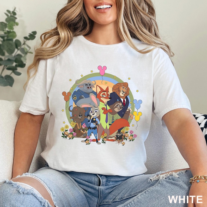 May include: White t-shirt with a vibrant cartoon illustration of Zootopia characters, such as Judy Hopps and Nick Wilde, set against a backdrop of flowers and balloons. The word "WHITE" is printed at the bottom right.
