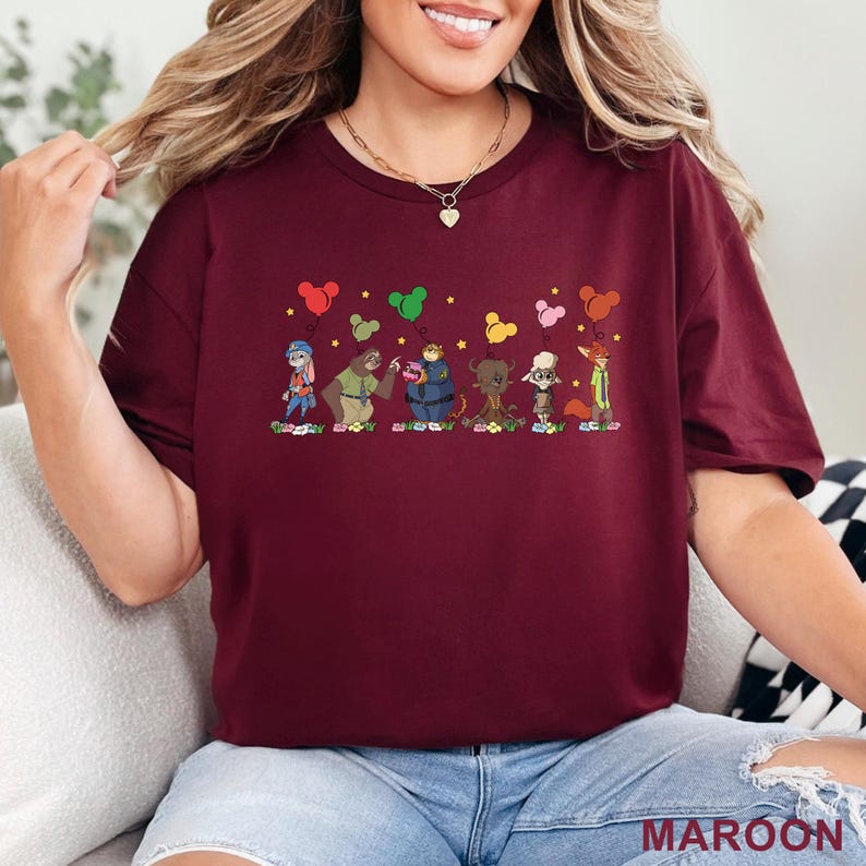 Puede incluir: Camiseta granate con una ilustraci&oacute;n de dibujos animados de personajes de animales, globos y estrellas. La palabra "MAROON" est&aacute; impresa en la esquina inferior derecha. El dise&ntilde;o presenta varios personajes de animales de dibujos animados.