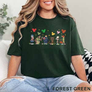 Puede incluir: Camiseta verde bosque con una colorida ilustraci&oacute;n de dibujos animados de varios personajes de animales sosteniendo globos. El texto "FOREST GREEN" est&aacute; impreso en la parte inferior de la camiseta. La camiseta es de un material suave.