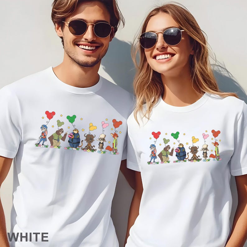 Puede incluir: Camisetas blancas con un dise&ntilde;o de dibujos animados colorido que presenta varios personajes de animales sosteniendo globos en forma de coraz&oacute;n. La palabra "WHITE" est&aacute; impresa en la parte inferior. Las camisetas las usan dos personas.