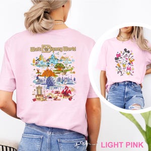 Op de afbeelding: Lichtroze T-shirts met Disney World-ontwerpen. E&eacute;n shirt toont een kleurrijke kaart van het park met de tekst "Walt Disney World". Het andere shirt toont Mickey Mouse, Minnie Mouse, Donald Duck, Daisy Duck, Goofy en Pluto.