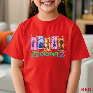 May include: A red t-shirt featuring the text "ZOOTOPIA 2" in green and a colorful graphic of characters from the movie. The shirt is short-sleeved and has a round neckline. The word "RED" is printed in the bottom right corner.