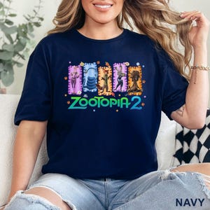 May include: Navy blue t-shirt featuring a colorful graphic of characters from the movie "Zootopia 2". The design includes the movie title in green and the word "NAVY" at the bottom. The shirt is made of a soft material.