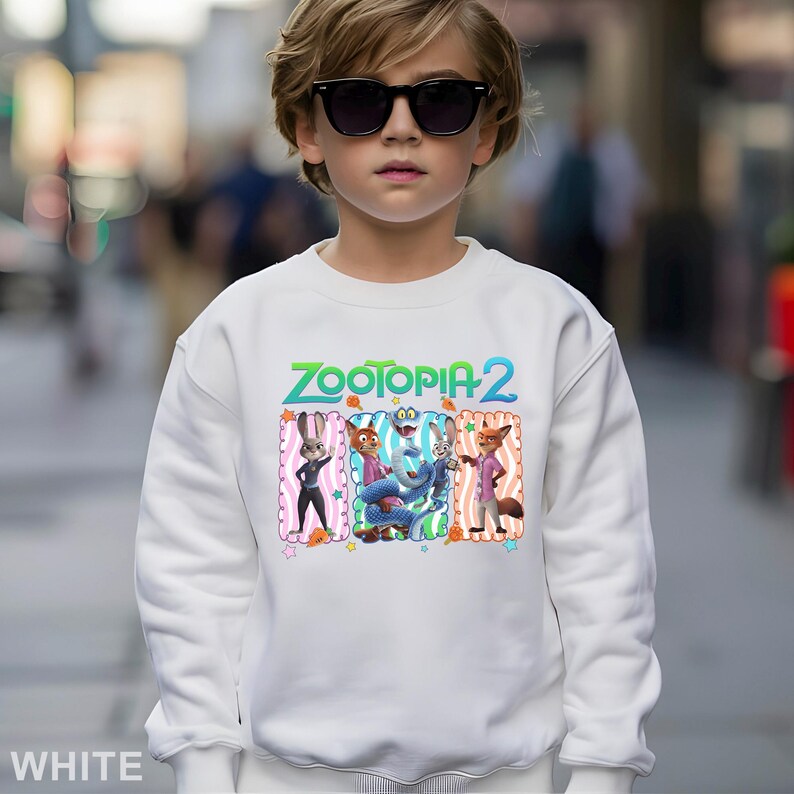 May include: White sweatshirt featuring the text "ZOOTOPIA 2" in green and blue. The sweatshirt has a colorful graphic of characters from the movie Zootopia. The word "WHITE" is printed at the bottom left.