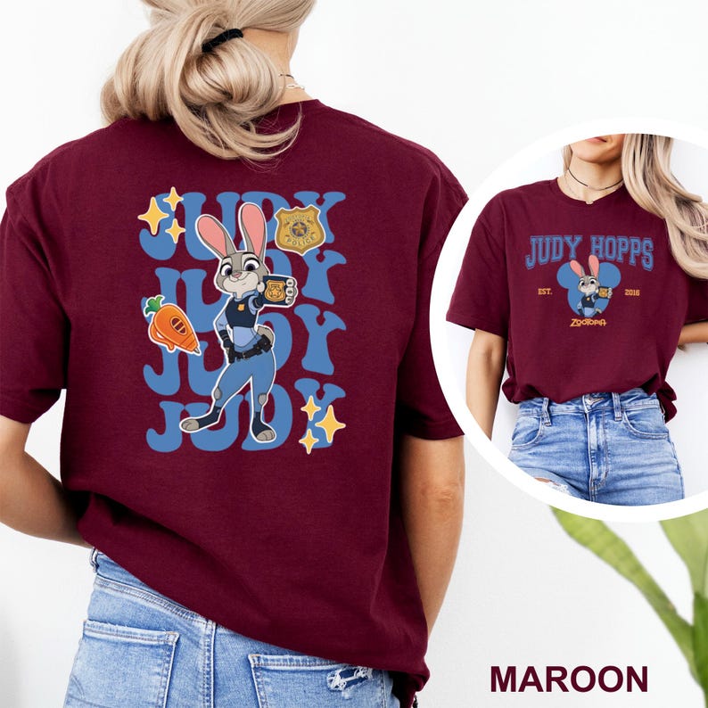 K&ouml;nnte beinhalten: Burgunderfarbenes T-Shirt mit einer Cartoon-Illustration von Judy Hopps aus Zootopia. Das Design zeigt Judy Hopps mit einer Kaffeetasse, einer Karotte und dem Text "Judy". Das Shirt hat auch ein Polizeiabzeichen.