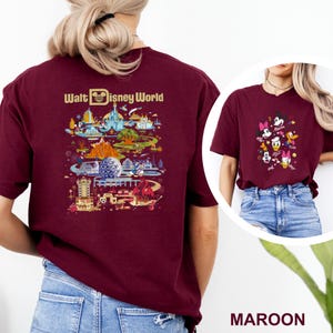 Op de afbeelding: Bordeauxrood T-shirt met een kleurrijke afbeelding van Disney World attracties en personages. De achterkant van het shirt toont de tekst "Walt Disney World" boven een gedetailleerde illustratie van het park. De voorkant van het shirt toont een afbeelding van Disney-personages.