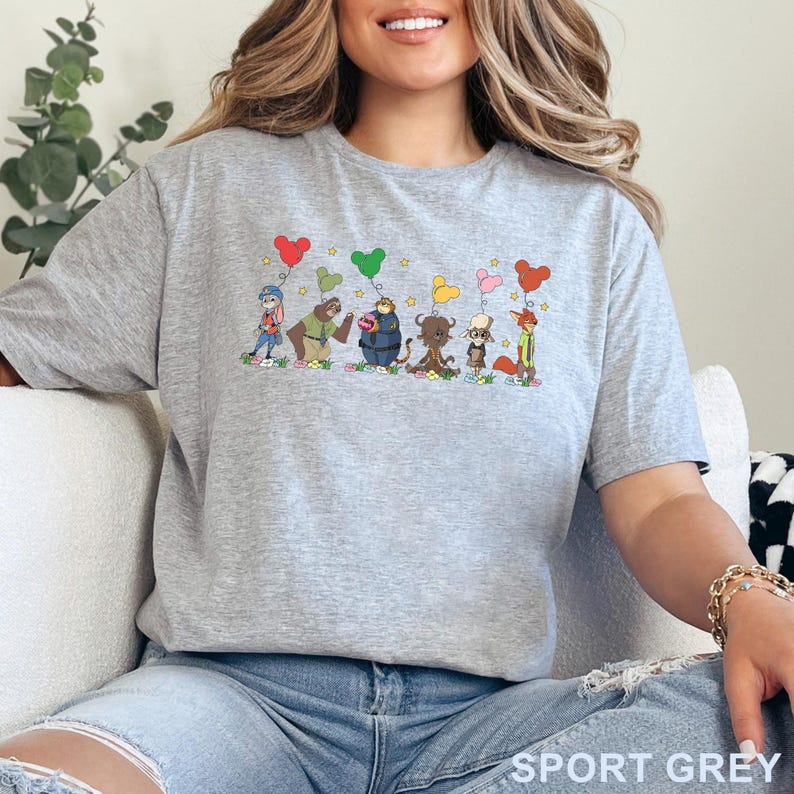 Puede incluir: Camiseta gris deportiva con un dise&ntilde;o de dibujos animados de personajes de animales sosteniendo globos en forma de coraz&oacute;n. Los personajes est&aacute;n de pie sobre hierba con flores. El texto "SPORT GREY" est&aacute; impreso en la parte inferior.