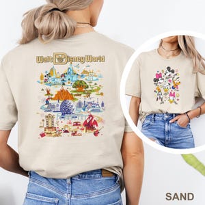 Op de afbeelding: Zandkleurig T-shirt met een afbeelding van Disney-personages en de tekst "Walt Disney World". De achterkant van het shirt toont een gedetailleerde illustratie van het themapark met verschillende attracties en personages.