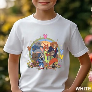 May include: White t-shirt with a vibrant cartoon graphic of animal characters. The design includes a rainbow, balloons, and flowers. The word "WHITE" is printed at the bottom right corner of the shirt.
