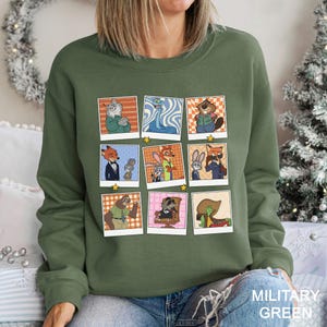 May include: Military green sweatshirt featuring a grid of cartoon character portraits. Each portrait is framed in a polaroid style with a star accent. The sweatshirt's color is labeled "MILITARY GREEN" in white text.