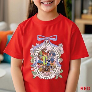 May include: A red t-shirt featuring a cartoon graphic of various animal characters within an oval frame, surrounded by flowers and a purple ribbon. The word "RED" is printed in the bottom right corner of the shirt.