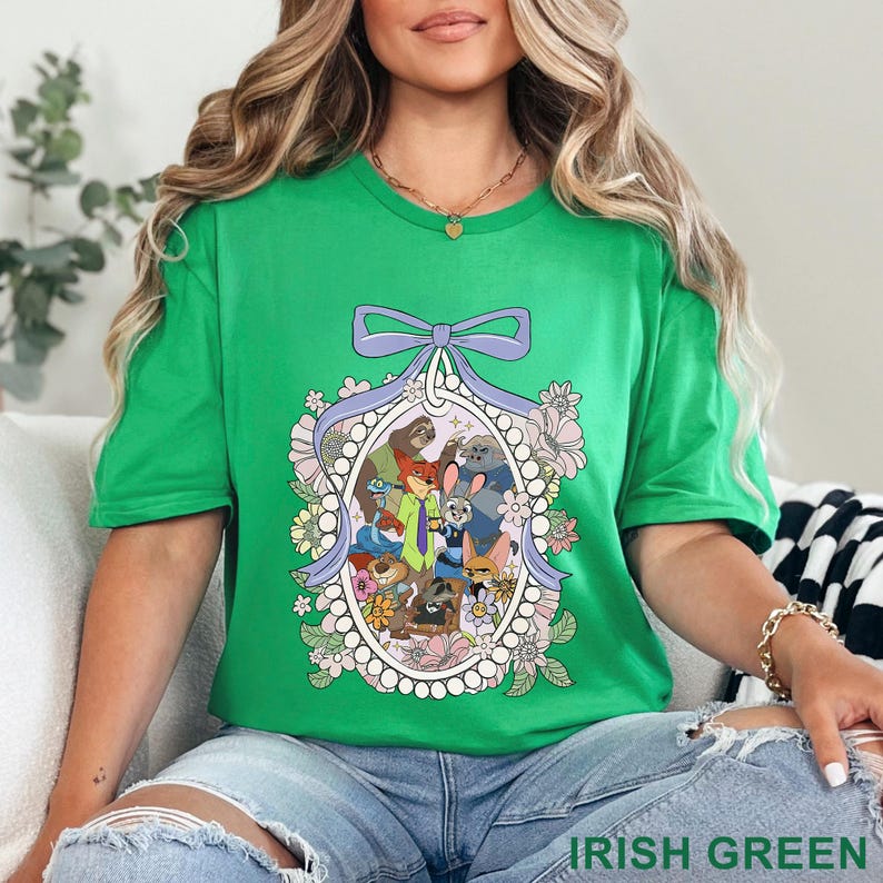 May include: A green t-shirt featuring a cartoon graphic of various animal characters within an oval frame, surrounded by flowers and a purple bow. The text "IRISH GREEN" is at the bottom of the image. The shirt is worn by a person.