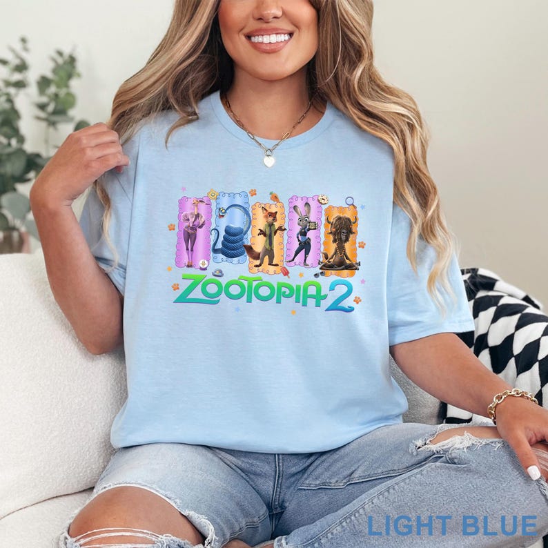 May include: Light blue t-shirt featuring the text "ZOOTOPIA 2" in green and a colorful graphic of characters from the movie. The shirt is a light blue color and is made of a soft material.