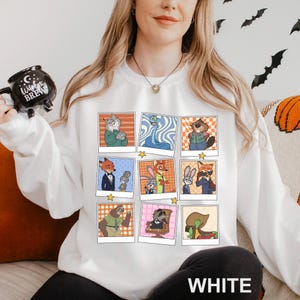 May include: White sweatshirt featuring a grid of cartoon character portraits in polaroid-style frames. The characters are in various poses and settings, with a star at the bottom of each frame. The word "WHITE" is printed in large, white letters at the bottom.