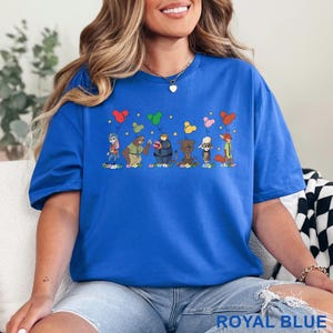 Puede incluir: Camiseta azul real con un dise&ntilde;o de dibujos animados caprichoso de personajes de animales sosteniendo globos en forma de coraz&oacute;n. El gr&aacute;fico incluye estrellas y flores. El texto "ROYAL BLUE" est&aacute; en la parte inferior de la camiseta.