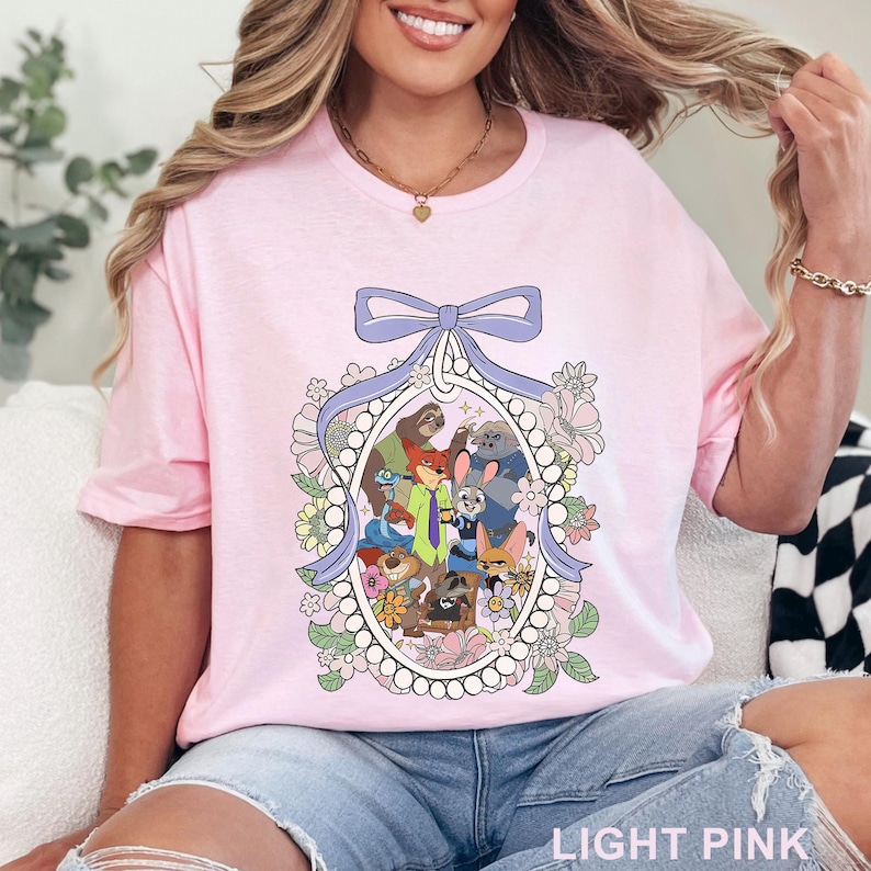 May include: Light pink t-shirt featuring a cartoon illustration of various animal characters within an oval frame, adorned with a bow and floral accents. The text "LIGHT PINK" is at the bottom of the shirt.