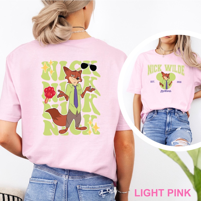 K&ouml;nnte beinhalten: Hellrosa T-Shirt mit einer Cartoon-Fuchsfigur mit Sonnenbrille, gr&uuml;nem Hemd und lila Krawatte. Auf der R&uuml;ckseite des Shirts steht "NICK WILDE" in einer gr&uuml;nen Retro-Schriftart. Das Shirt ist hellrosa.