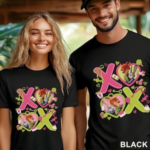 Puede incluir: Camisetas negras con un dise&ntilde;o gr&aacute;fico colorido con los personajes Nick Wilde y Judy Hopps de Zootopia. El dise&ntilde;o incluye elementos rosas y verdes, corazones y las letras X y O. La palabra "BLACK" est&aacute; impresa en la parte inferior derecha.