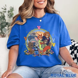 May include: Royal blue t-shirt with a cartoon graphic of animal characters, including a fox and a rabbit, set against a rainbow and floral background. The text "ROYAL BLUE" is at the bottom. The design is vibrant and eye-catching.