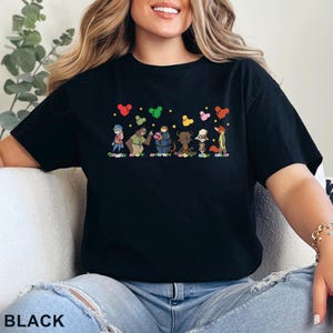 Puede incluir: Camiseta negra con un dise&ntilde;o de dibujos animados de personajes de animales y formas de coraz&oacute;n y estrella. La palabra "BLACK" est&aacute; impresa en la parte inferior de la camiseta.