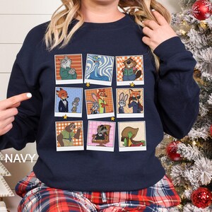 May include: Navy blue sweatshirt featuring a grid of nine cartoon character portraits. Each portrait is framed with a white border and a gold star. The characters are anthropomorphic animals in various outfits and poses. The word "NAVY" is printed on the left side.