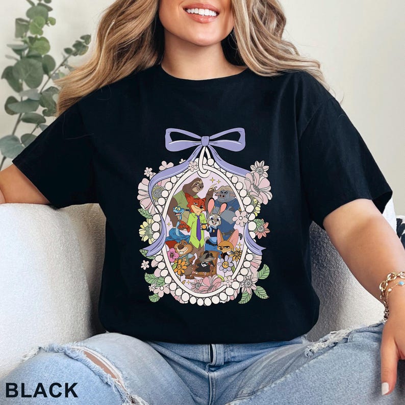 May include: Black t-shirt featuring a colorful cartoon illustration of various animal characters within an oval frame, surrounded by flowers and a bow. The word "BLACK" is printed at the bottom of the shirt.